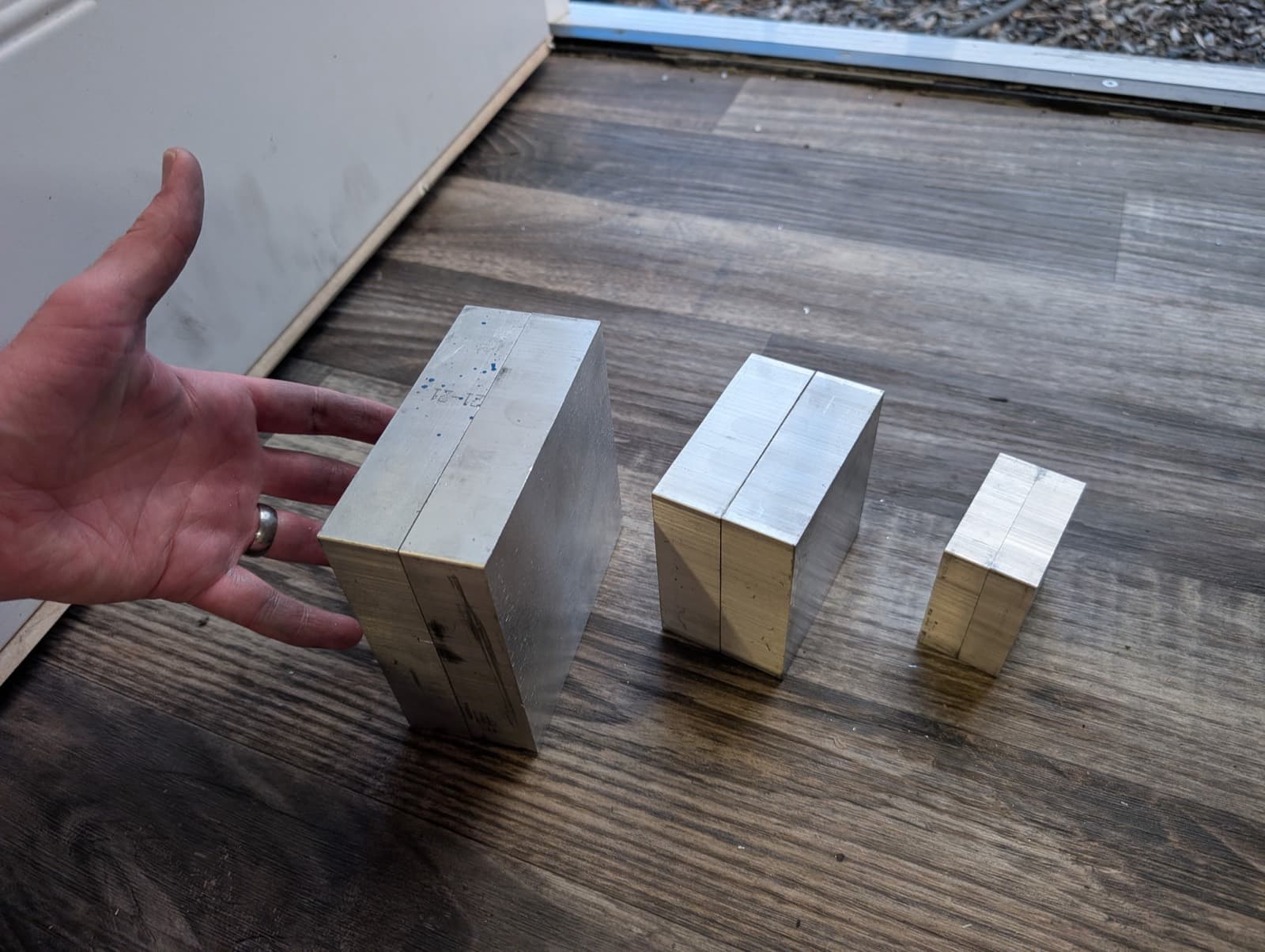 Small, medium, and large aluminum mold blanks side by side with a hand for scale