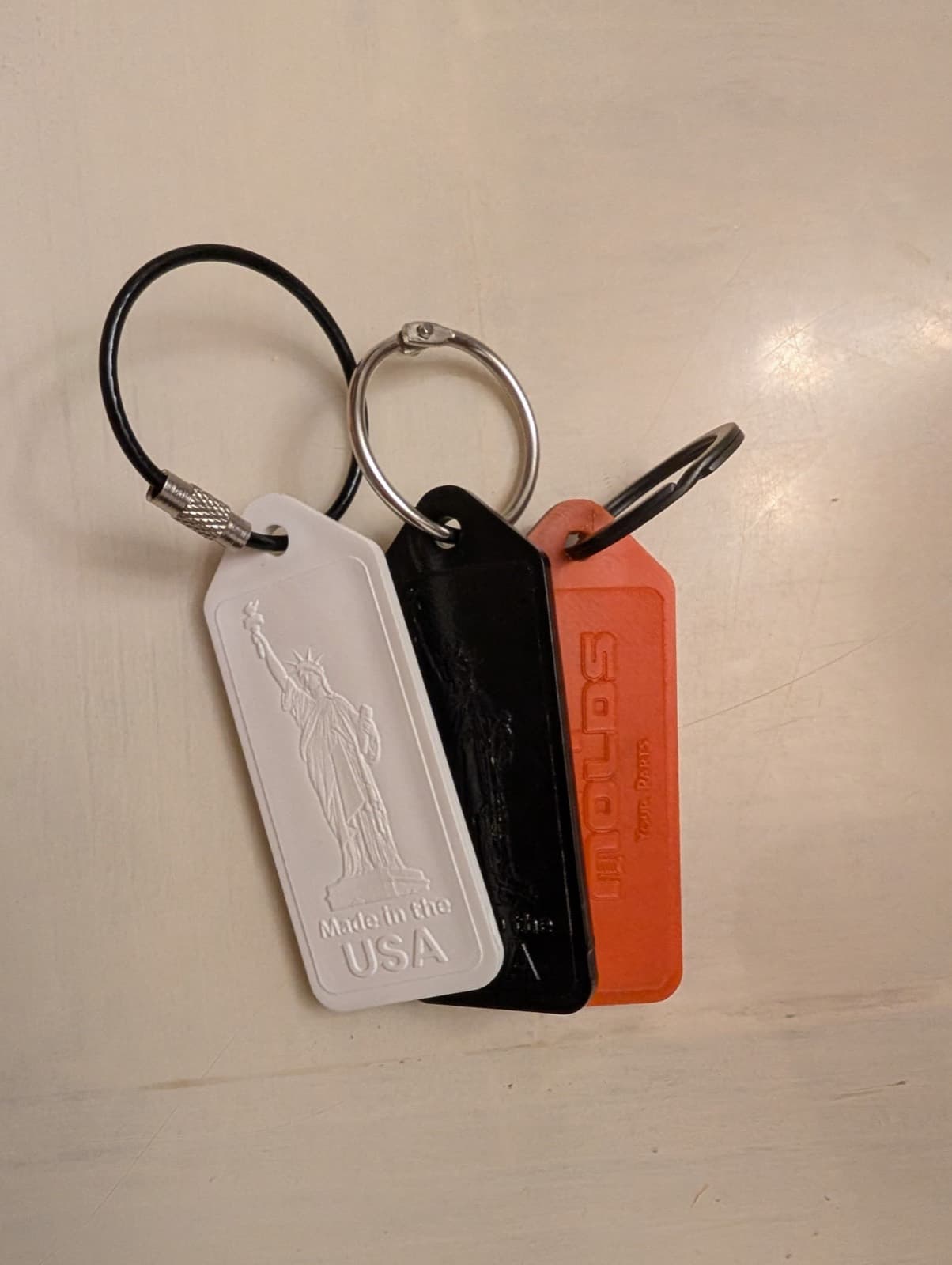 Three identical keychains molded in white, black, and orange plastic